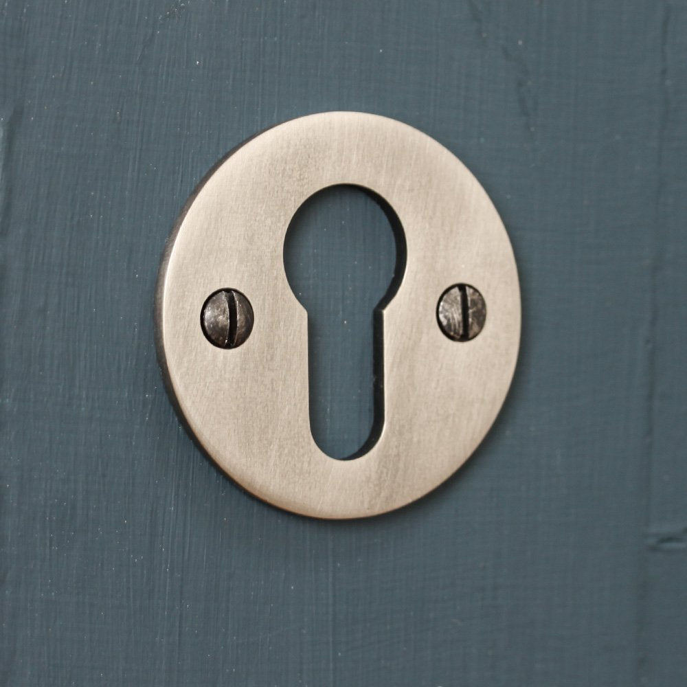 Solid brass circular escutcheon with antique nickel finish, against plain background.
