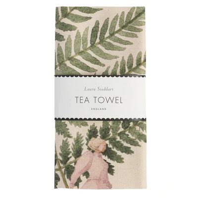 A tea towel with a floral design featuring ferns and leaves on a beige background, with a label that reads 'Laura Stoddart Tea Towel' and 'England'.