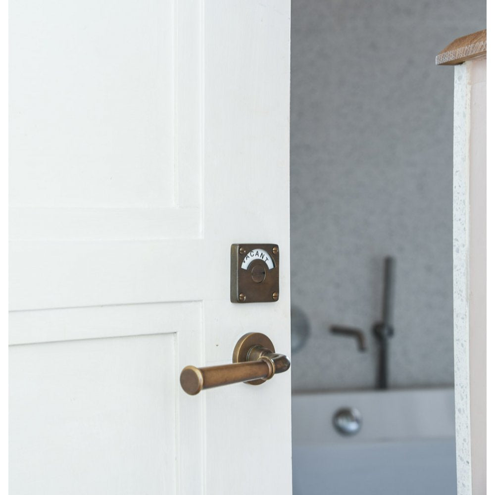 Distressed antique brass Grace Lever Handles paired with our Vacant/Engaged Lock on bathroom door.