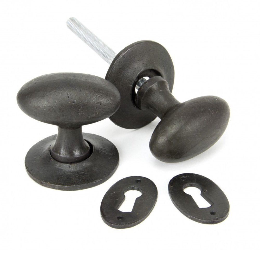A set of oval black beeswax door knobs with a pair of keyhole escutcheons in a beeswax finish