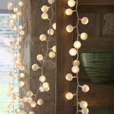 White pom pom fairy lights hanging across wall and shelving