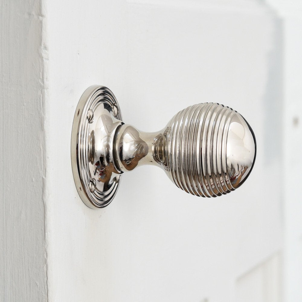 Solid brass Reeded Beehive Door Knobs in Polished Nickel finish on white door.
