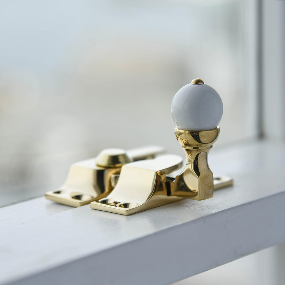 A Sash Window Fastener with White Knob in Polished Brass fitted to a sash window