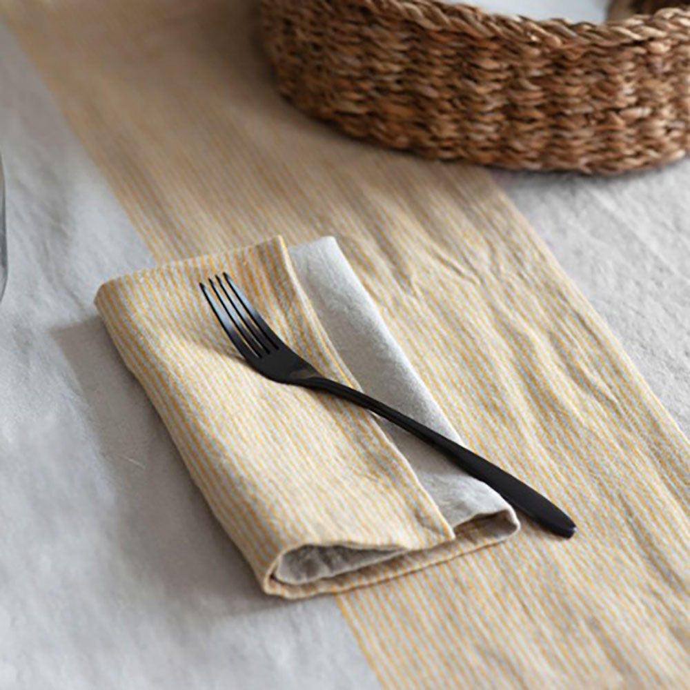 Striped linen napkins in yellow and cream on a striped table runner with a black fork