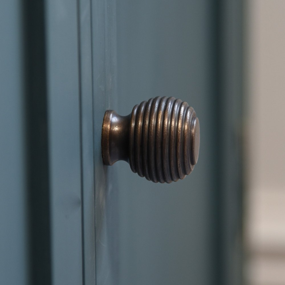 Side view of Queen Anne Beehive Cabinet Knob in Distressed Antique Brass on teal cupboard door.