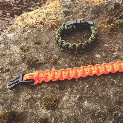 survival bracelets in green and orange sat on rock