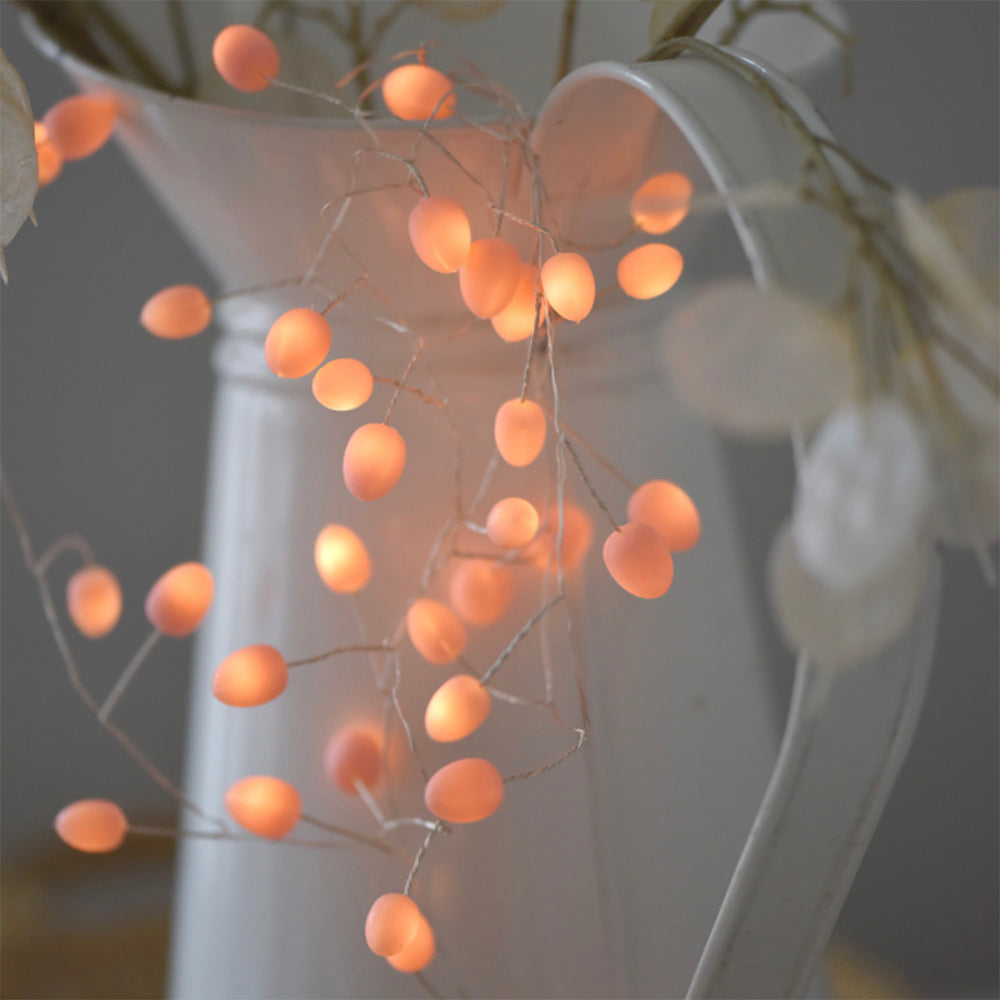 Teardrop Shaped Fairy Lights in Pink Wrapped Around Jug and Foliage