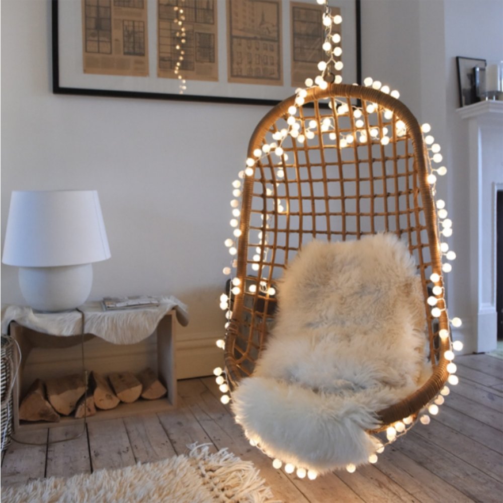 Light up white pom pom lights on string draped around rattan swing chair with sheepskin rug