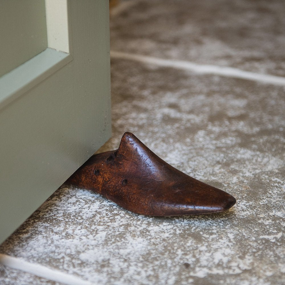 A wooden shoe last door stop wedged under a door. A section of the heel has been sliced off to enable the door stop to be pushed against the door