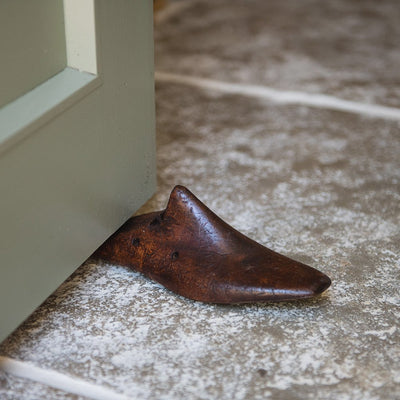 A wooden shoe last door stop wedged under a door. A section of the heel has been sliced off to enable the door stop to be pushed against the door